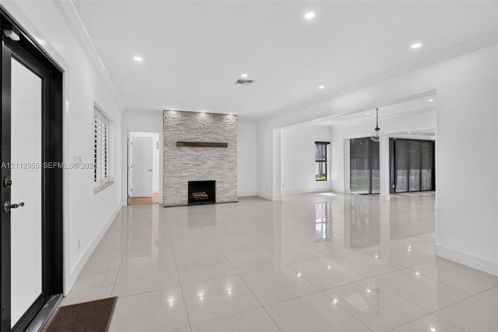549 NE 12th Avenue, Fort Lauderdale, FL 33301 Open-concept interior featuring large-format polished tile flooring, stone-veneer fireplace with a wood mantel, recessed ceiling lighting, and floor-to-ceiling glass sliding doors