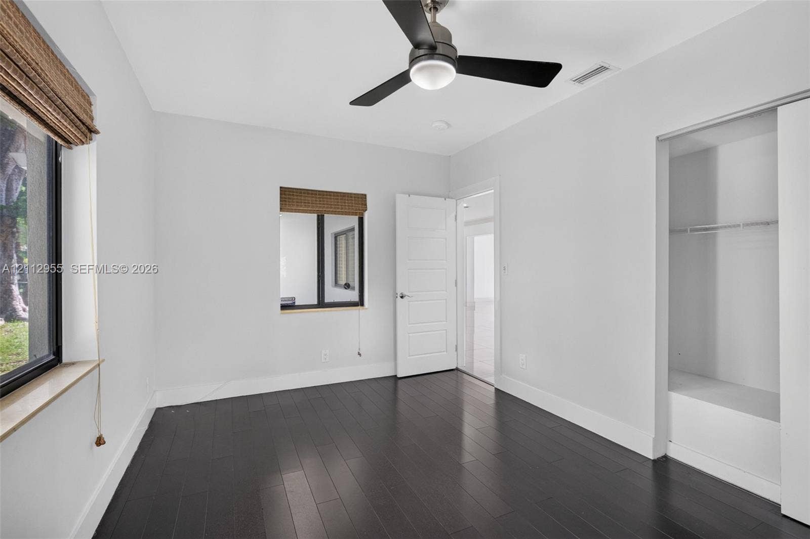 549 NE 12th Avenue, Fort Lauderdale, FL 33301 Room featuring dark wood-finish flooring, a contemporary matte black ceiling fan with integrated lighting, two windows with woven shades, and a built-in closet with sliding doors