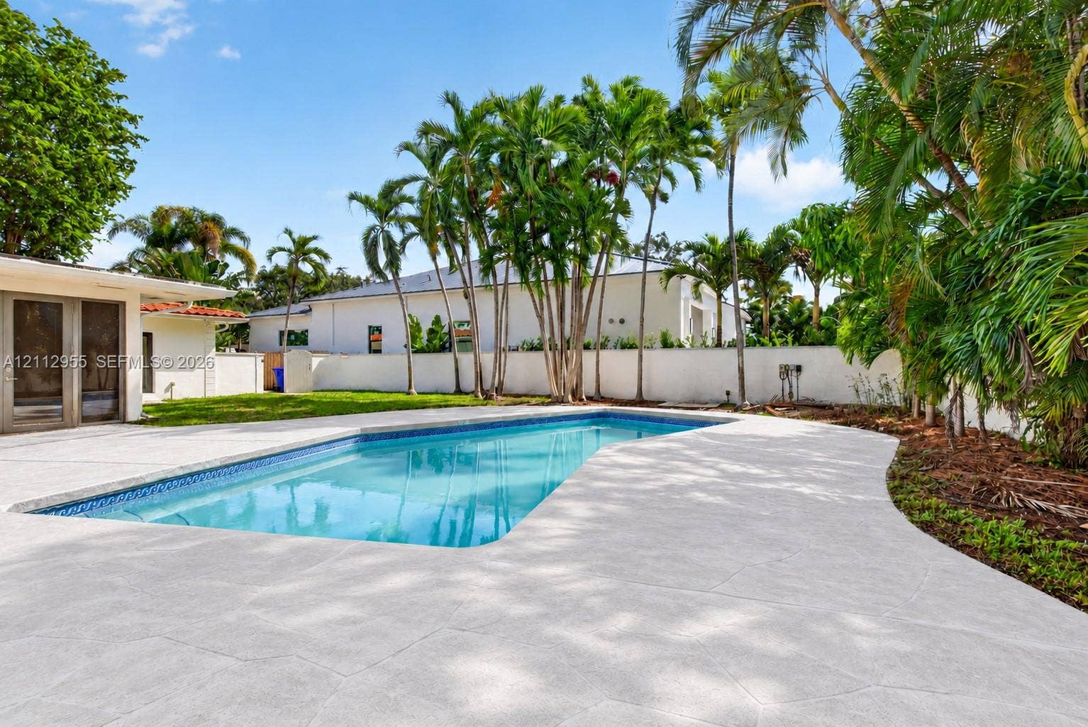 549 NE 12th Avenue, Fort Lauderdale, FL 33301 In-ground swimming pool featuring a textured concrete deck, privacy wall, manicured lawn, and mature palm trees