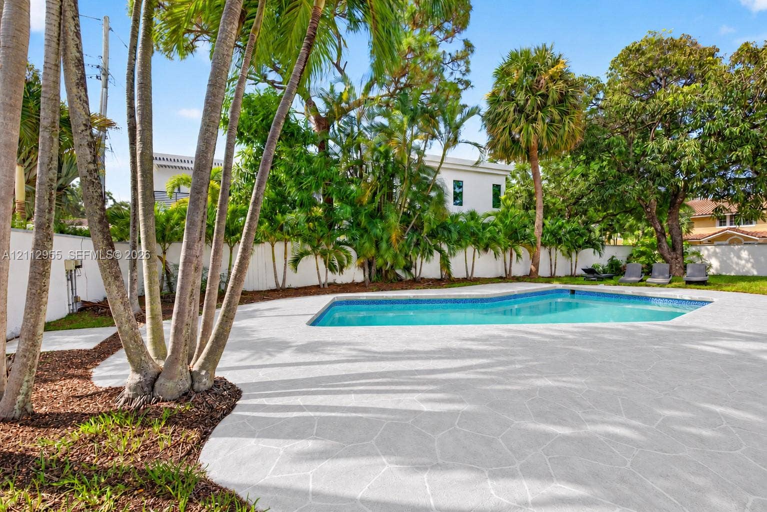 549 NE 12th Avenue, Fort Lauderdale, FL 33301 Outdoor space featuring a swimming pool, expansive stone-paver patio, perimeter privacy fencing, and mature palm trees