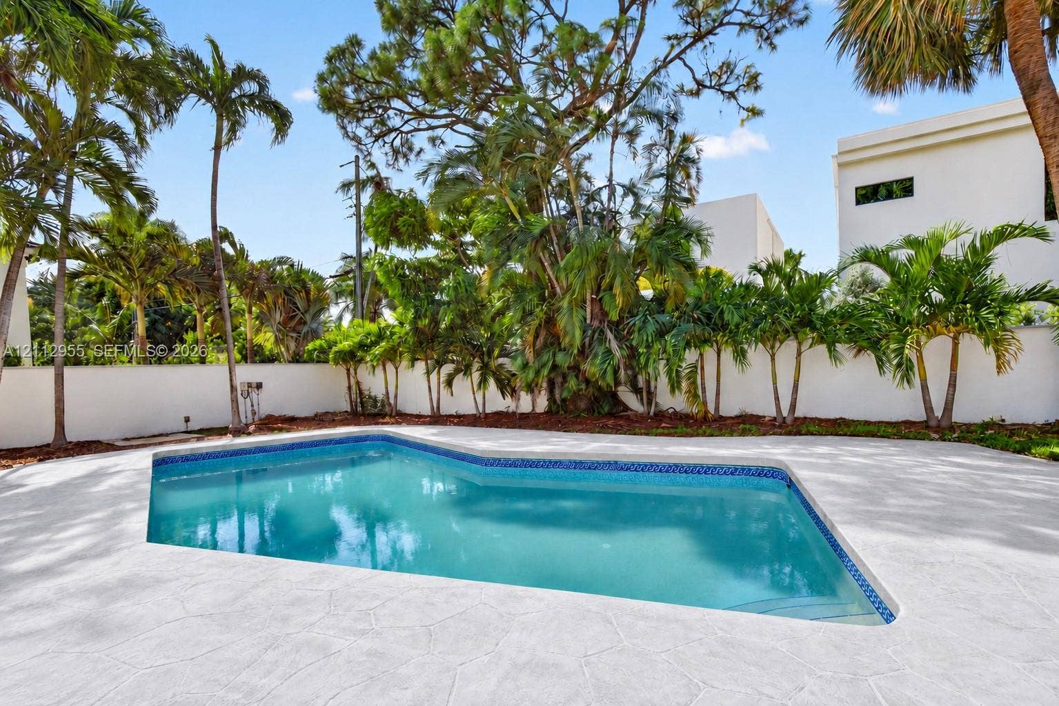 549 NE 12th Avenue, Fort Lauderdale, FL 33301 In-ground swimming pool featuring a patterned tile border, concrete deck, solid perimeter wall, and mature palm trees
