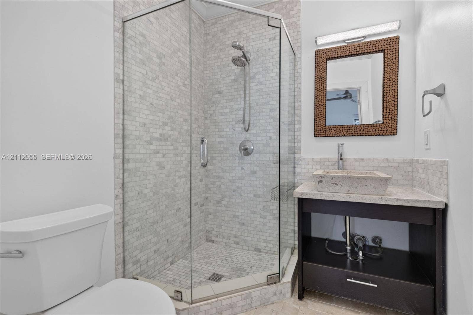 549 NE 12th Avenue, Fort Lauderdale, FL 33301 Corner shower enclosure with glass panels, stone-tiled walls, and a handheld showerhead