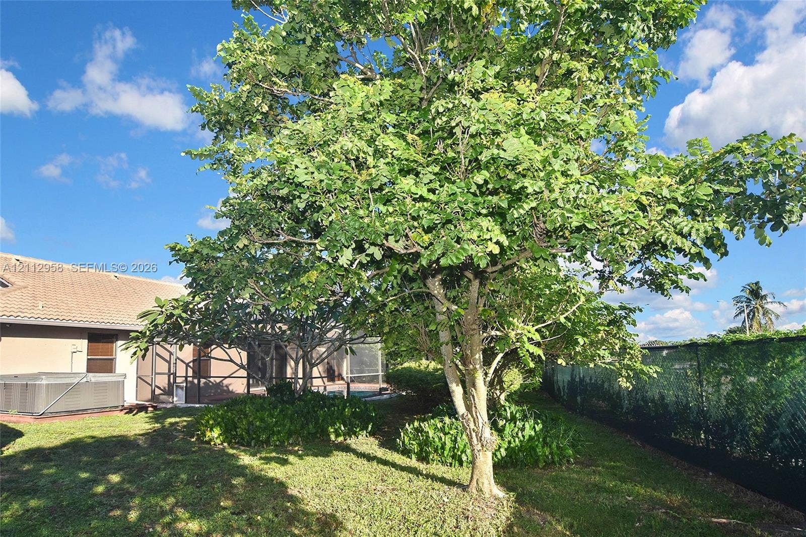 Backyard featuring mature trees, a screened-in lanai, and a tiled roof exterior