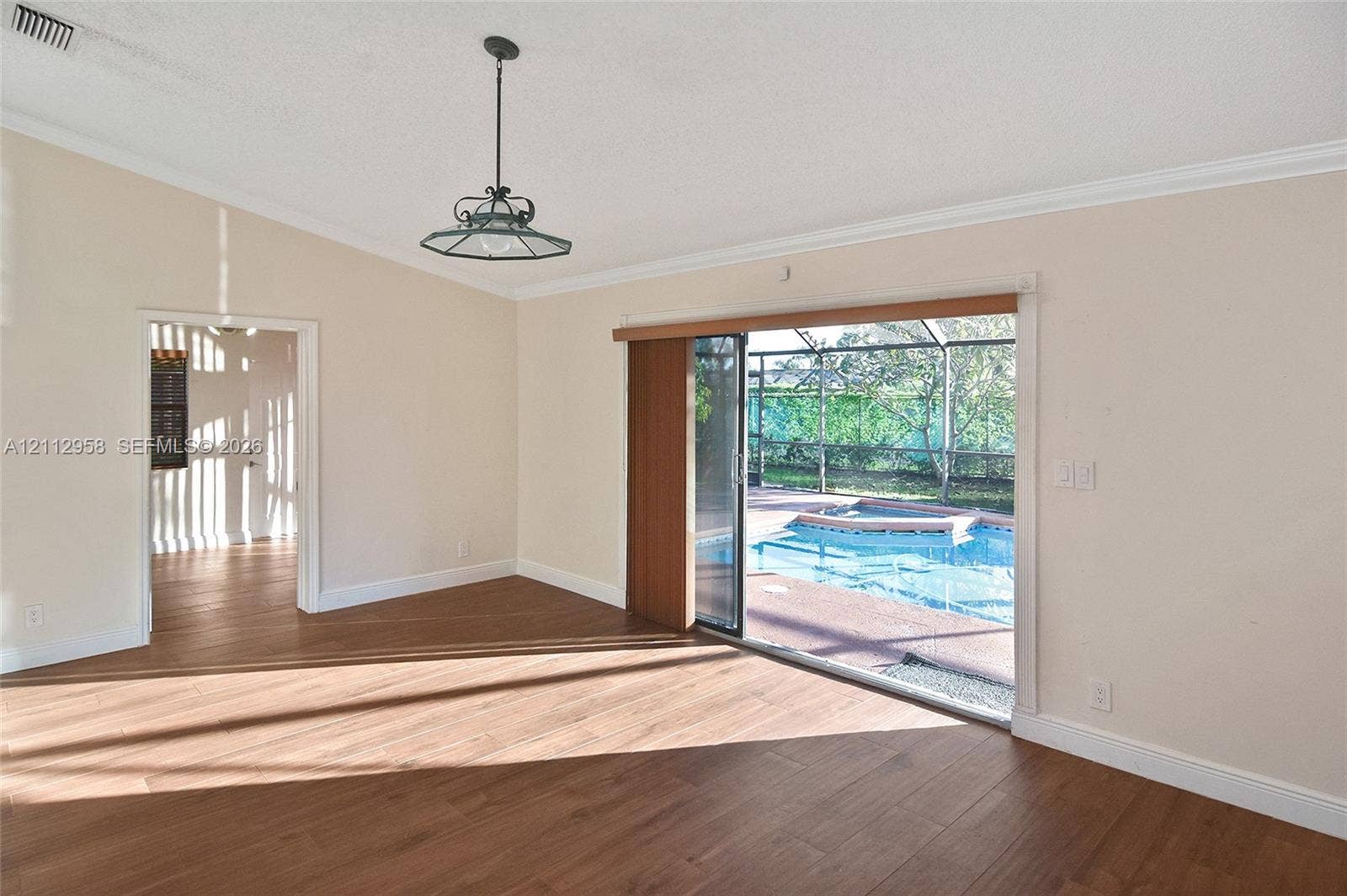 Vaulted ceiling room featuring wood-finish flooring, a decorative metal pendant light, crown molding, and sliding glass doors opening to a screened-in pool area