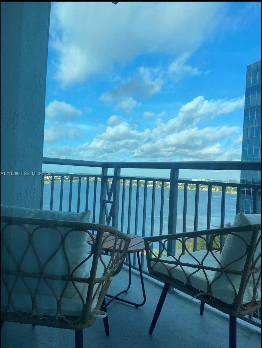 Covered balcony featuring metal railings and concrete flooring with water and skyline scenery
