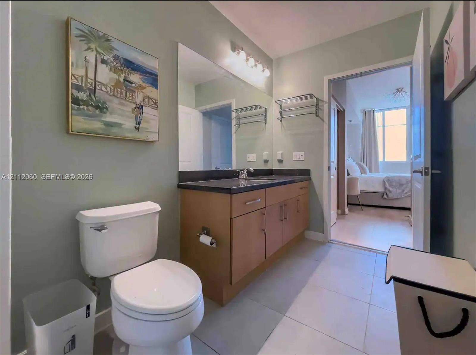 Bathroom featuring a vanity with light-tone cabinetry, dark surface countertop, integrated sink, wall-spanning vanity mirror, and multi-bulb fixed lighting