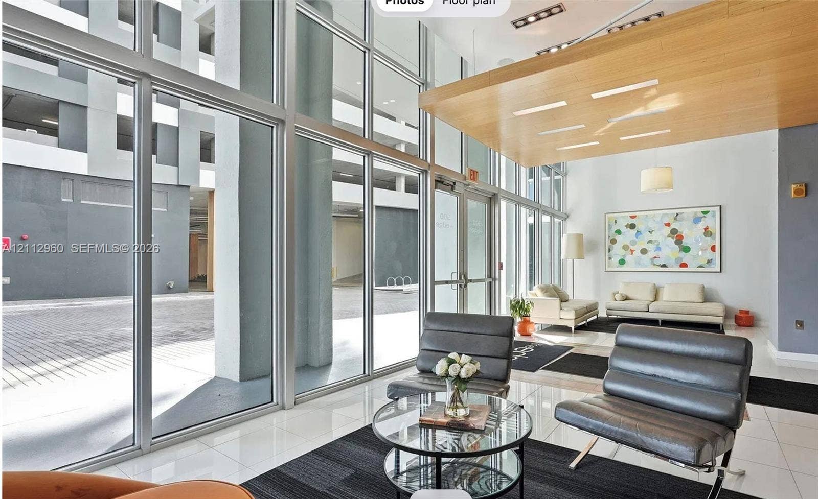 Floor-to-ceiling glass curtain walls, soaring double-height ceilings, light-tone wood-finish architectural paneling, recessed lighting, and polished stone-finish flooring