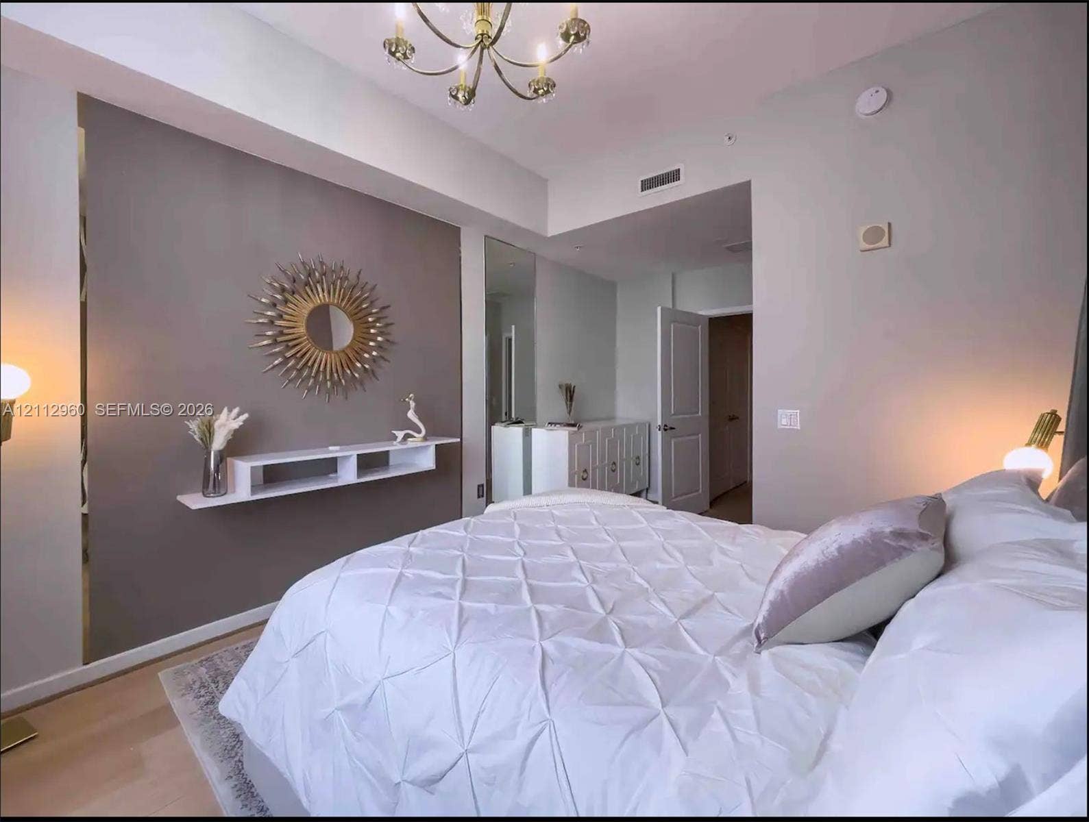 Accent wall with a mounted white floating shelf, multi-arm metal chandelier, and wood-finish flooring