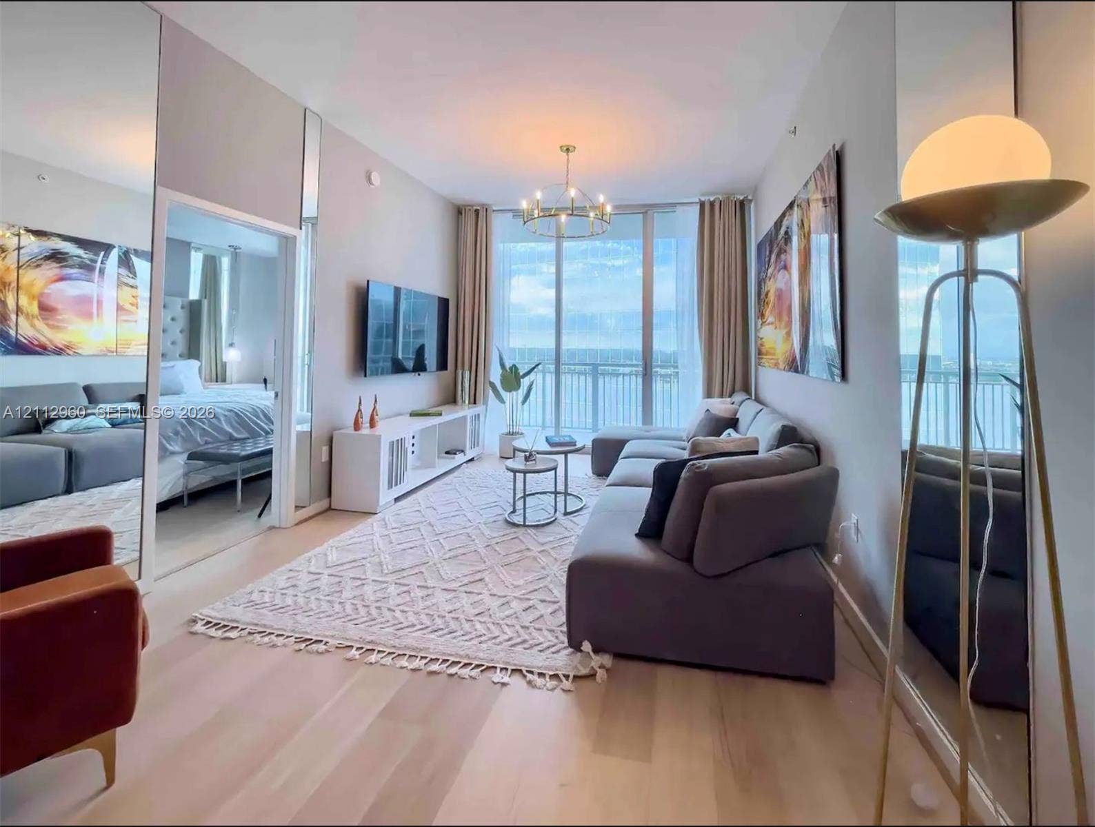 Floor-to-ceiling glass paneling, wood-finish flooring, full-height wall mirrors, custom multi-arm chandelier, and balcony access