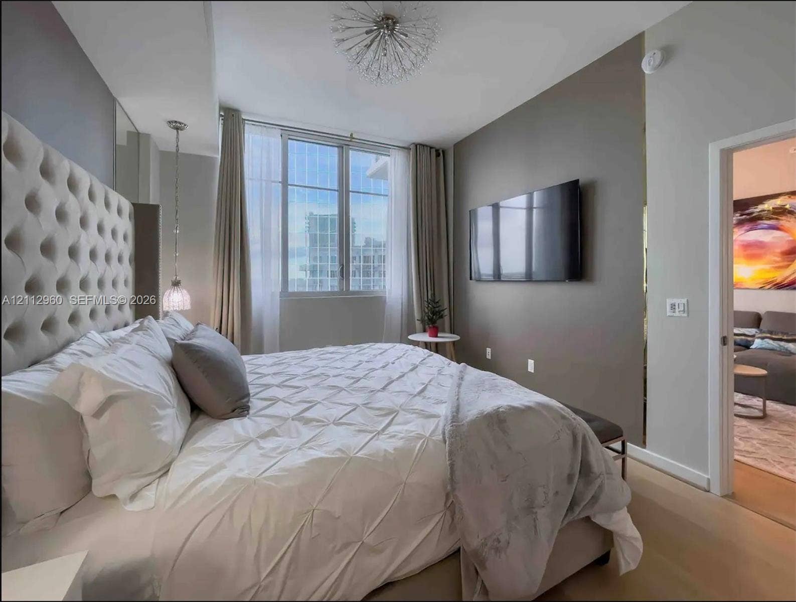 Floor-to-ceiling windows, sculptural ceiling lighting fixture, pendant lighting, wall-mounted electrical interface, and wood-finish flooring