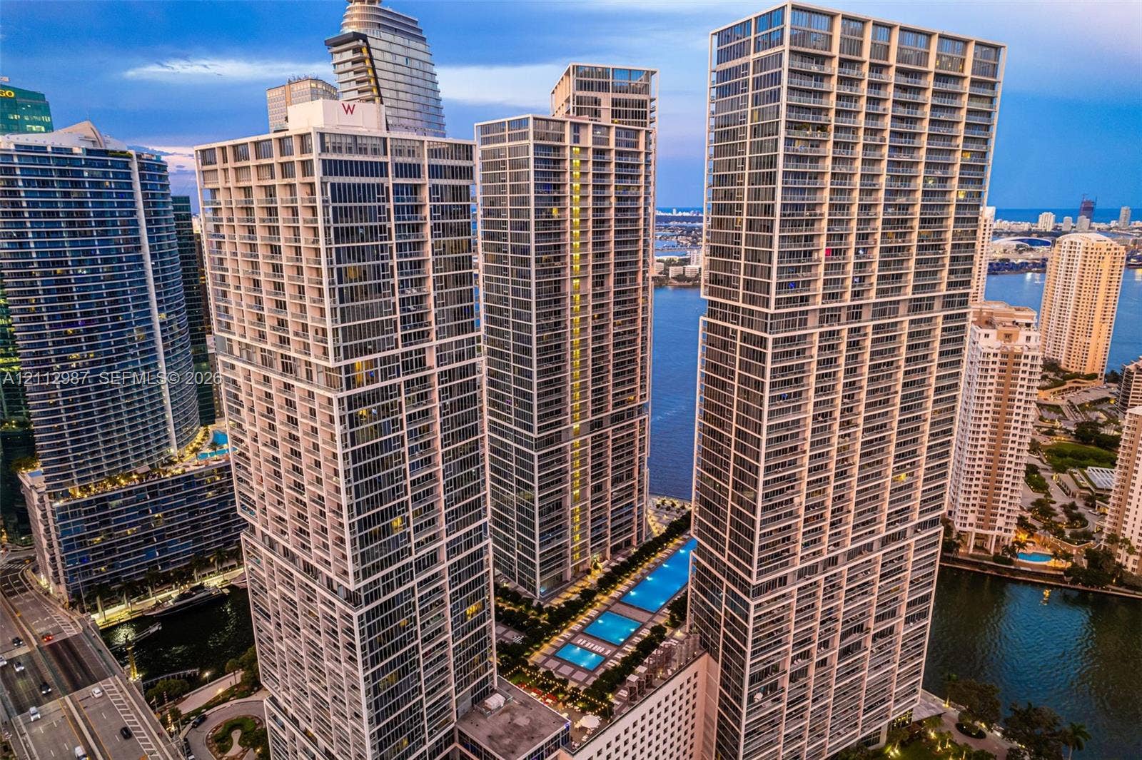 High-rise urban towers featuring glass facades, multiple private balconies, and an elevated multi-pool deck overlooking the waterfront