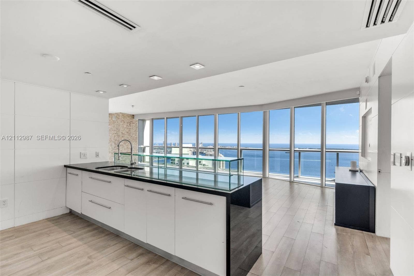 Kitchen featuring a central island with a dark stone countertop, integrated glass backsplash, white cabinetry with metal hardware, floor-to-ceiling windows, and wood-finish flooring
