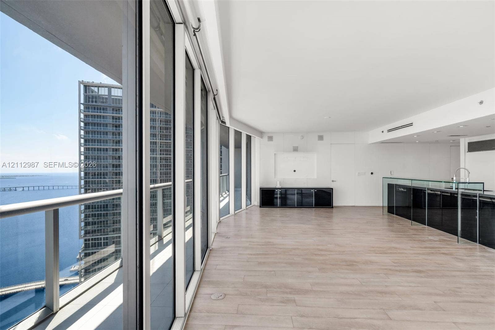 Floor-to-ceiling glass panel walls, wood-finish flooring, built-in black cabinetry, and a glass-partitioned kitchen area
