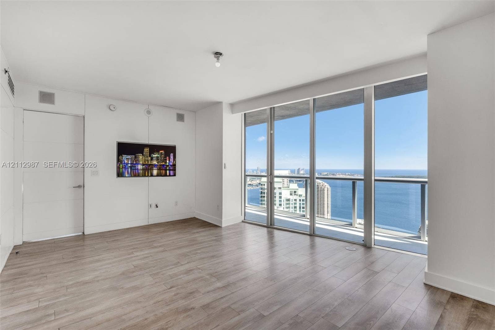 Floor-to-ceiling windows, private glass-railed balcony, wood-finish flooring, and minimalist white walls