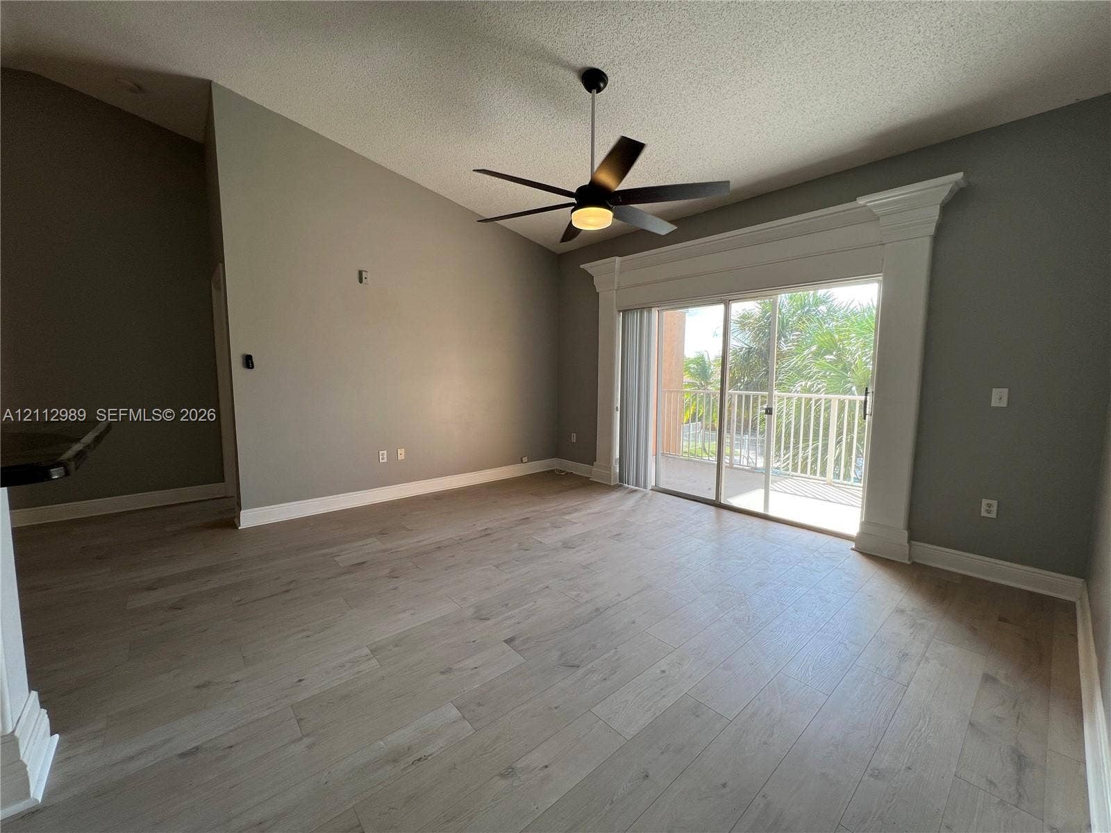 Vaulted ceilings, wood-finish flooring, central ceiling fan, and sliding glass doors encased in decorative molding with access to an exterior balcony