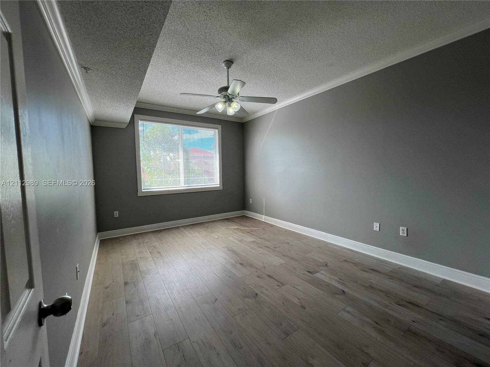 Room featuring wood-finish flooring, crown molding, a ceiling fan with integrated lighting, and a window with white trim
