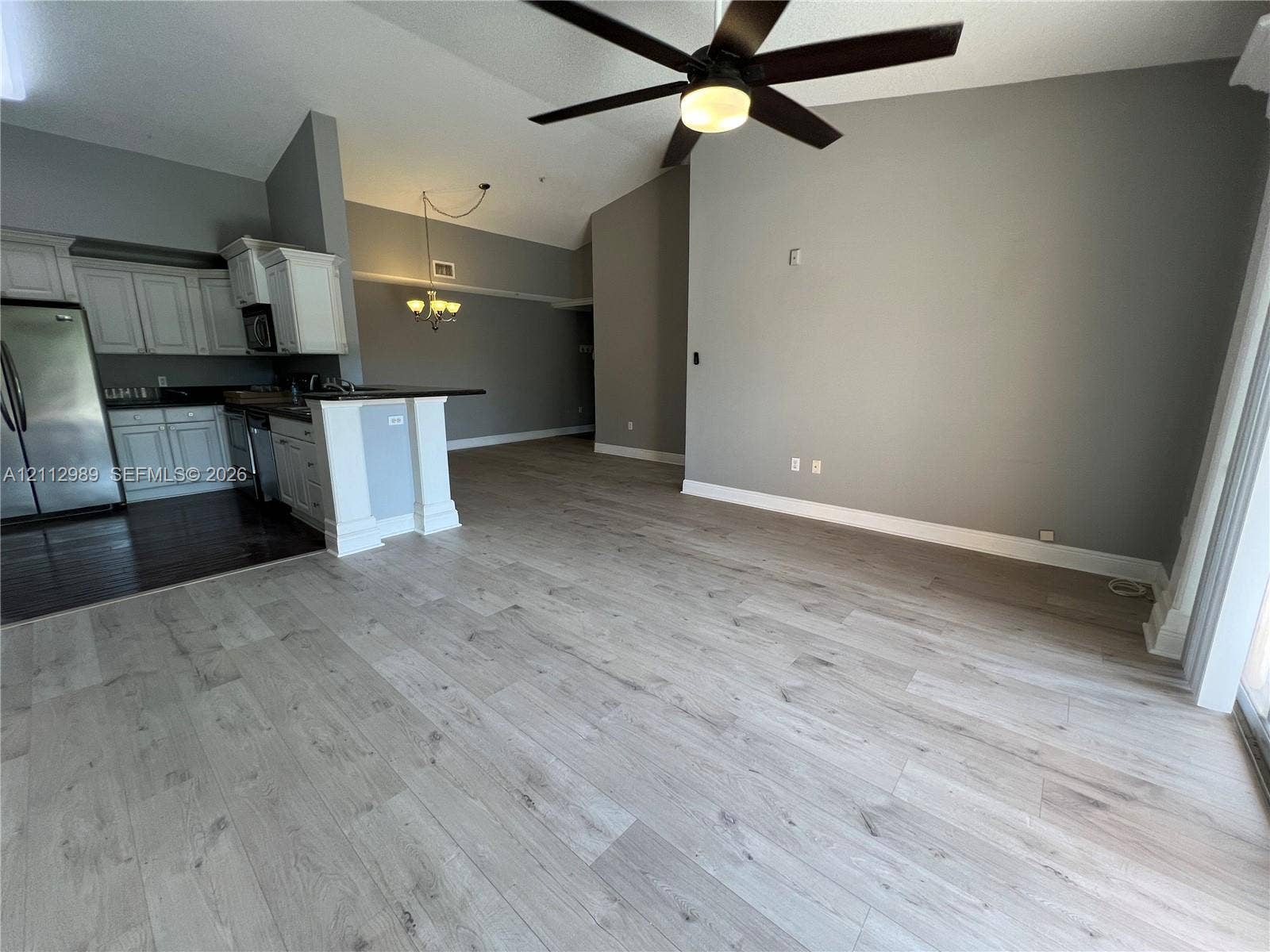 Vaulted ceilings with a multi-blade ceiling fan, wood-finish flooring, and white cabinetry featuring a kitchen peninsula