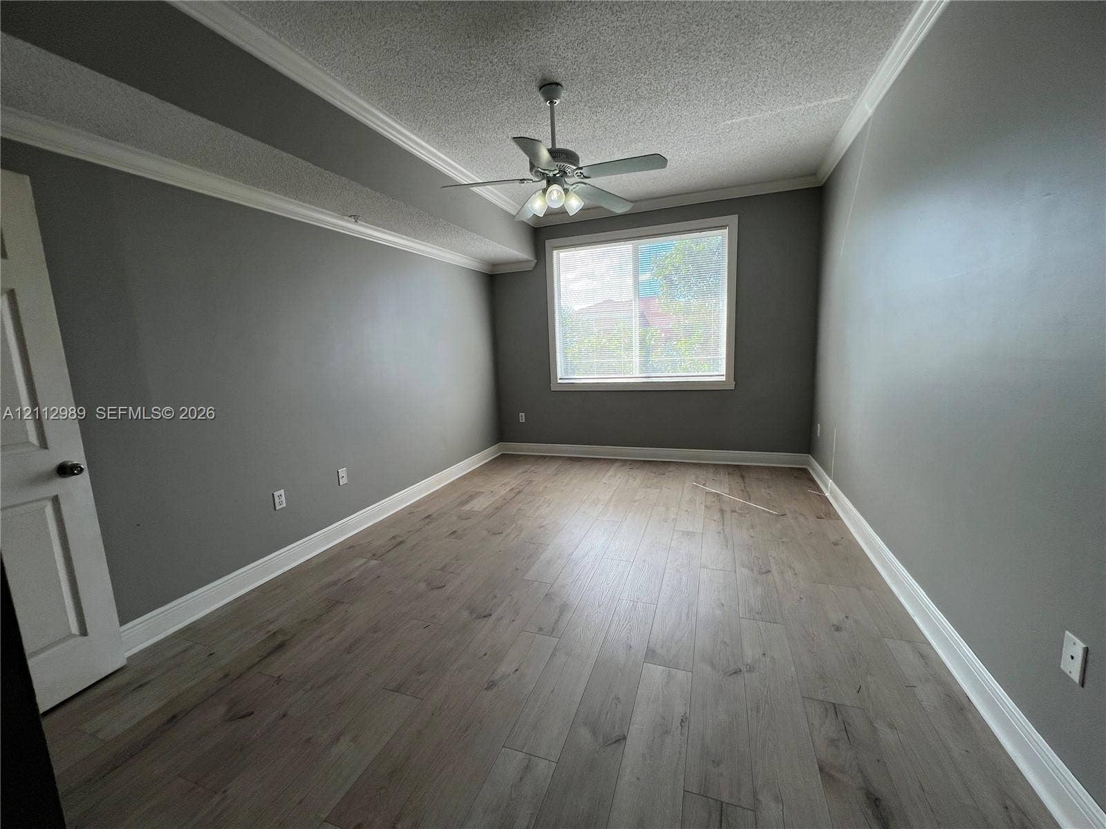 Room featuring wood-finish flooring, crown molding, a ceiling fan with integrated lighting, and a single-pane window