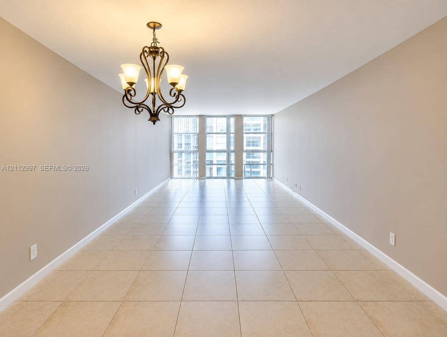 Spacious room featuring neutral-toned tile flooring, floor-to-ceiling windows, and a decorative multi-light metal chandelier