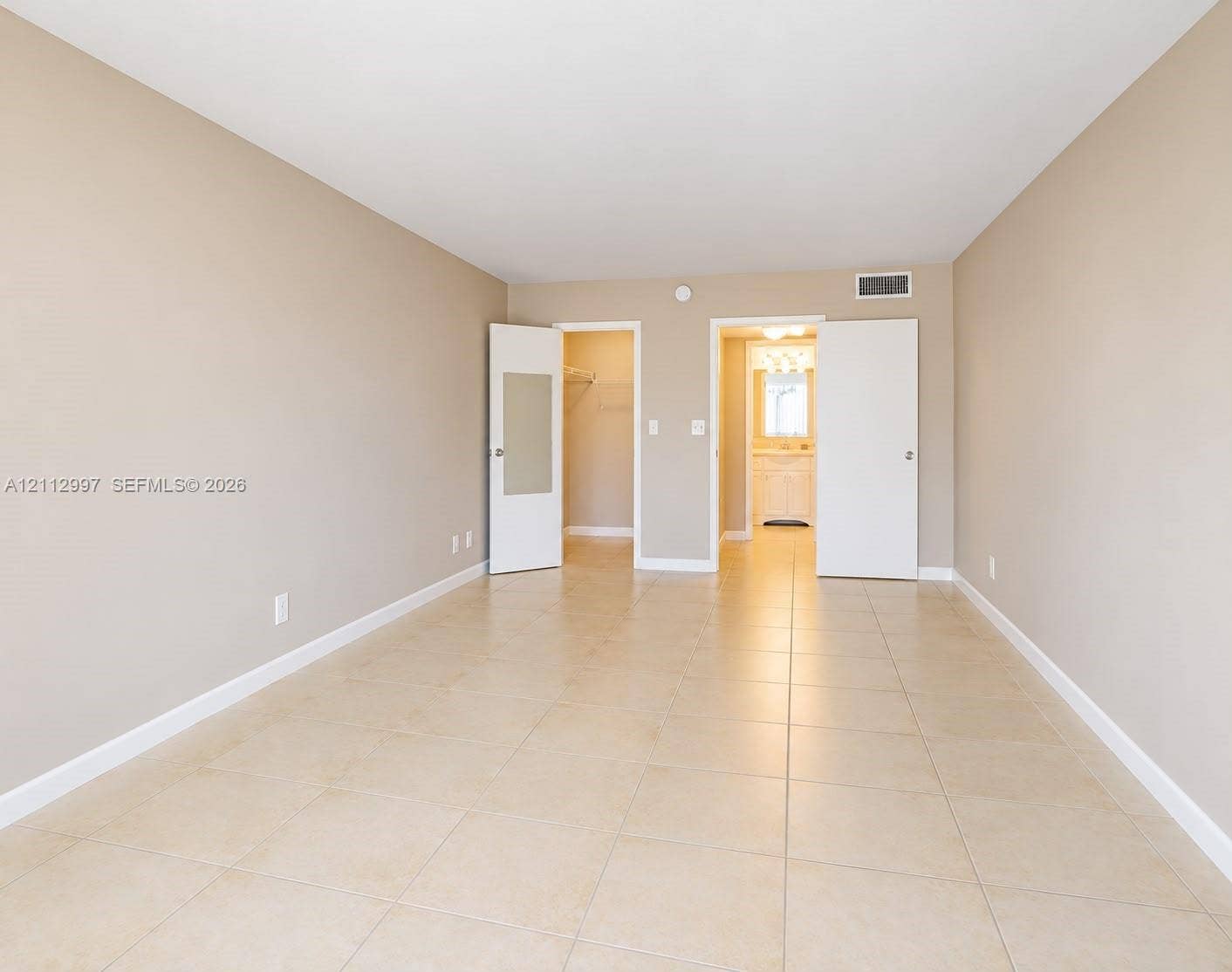Neutral-toned room featuring large-format ceramic tile flooring, two white interior doors, and a walk-in closet