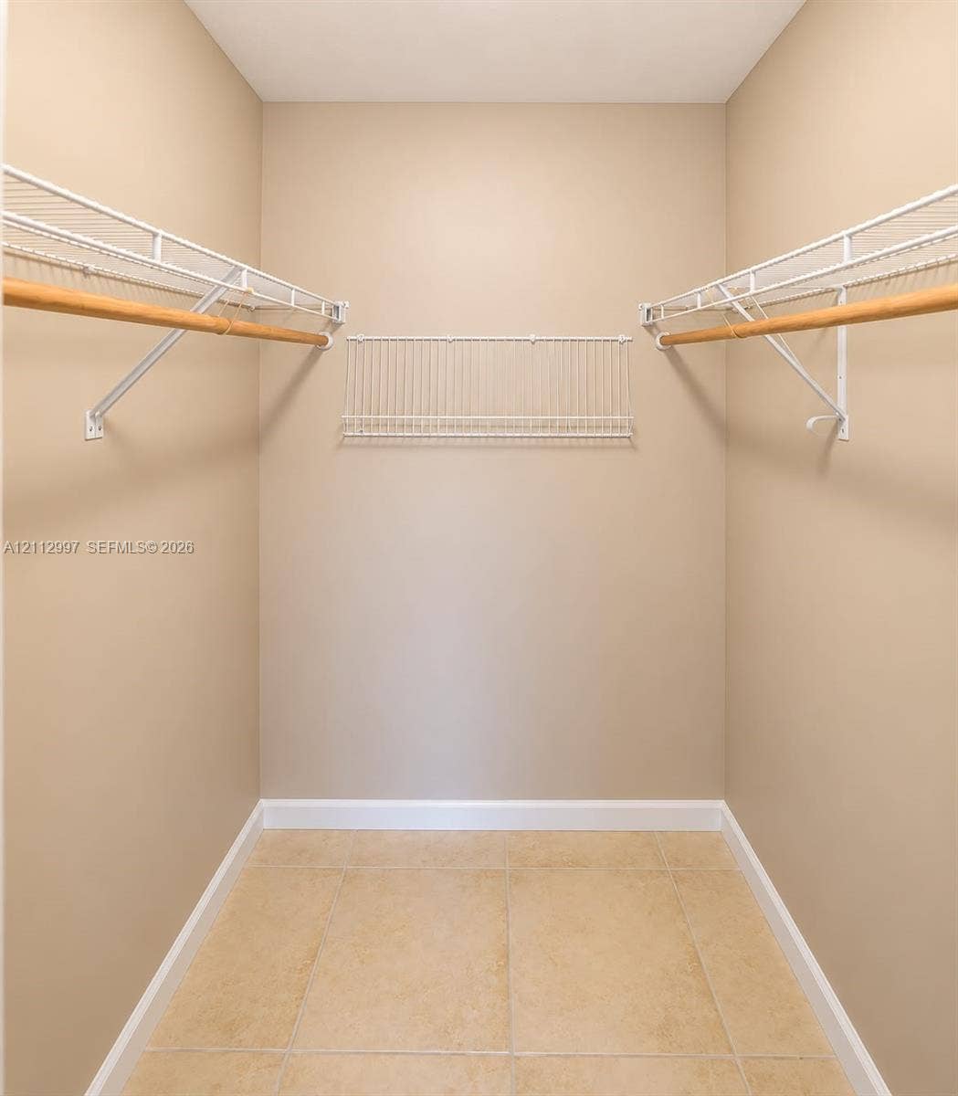 Walk-in storage space featuring ceramic tile flooring and multi-level white wire shelving with wood-finish garment rods