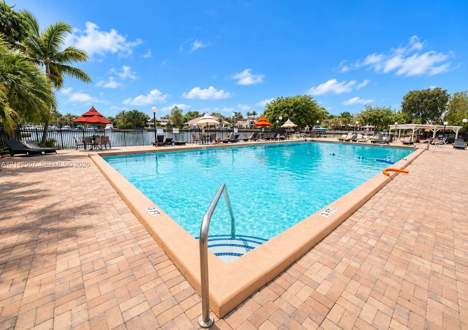 Large in-ground swimming pool featuring a brick paver deck, metal safety fencing, and stair entry