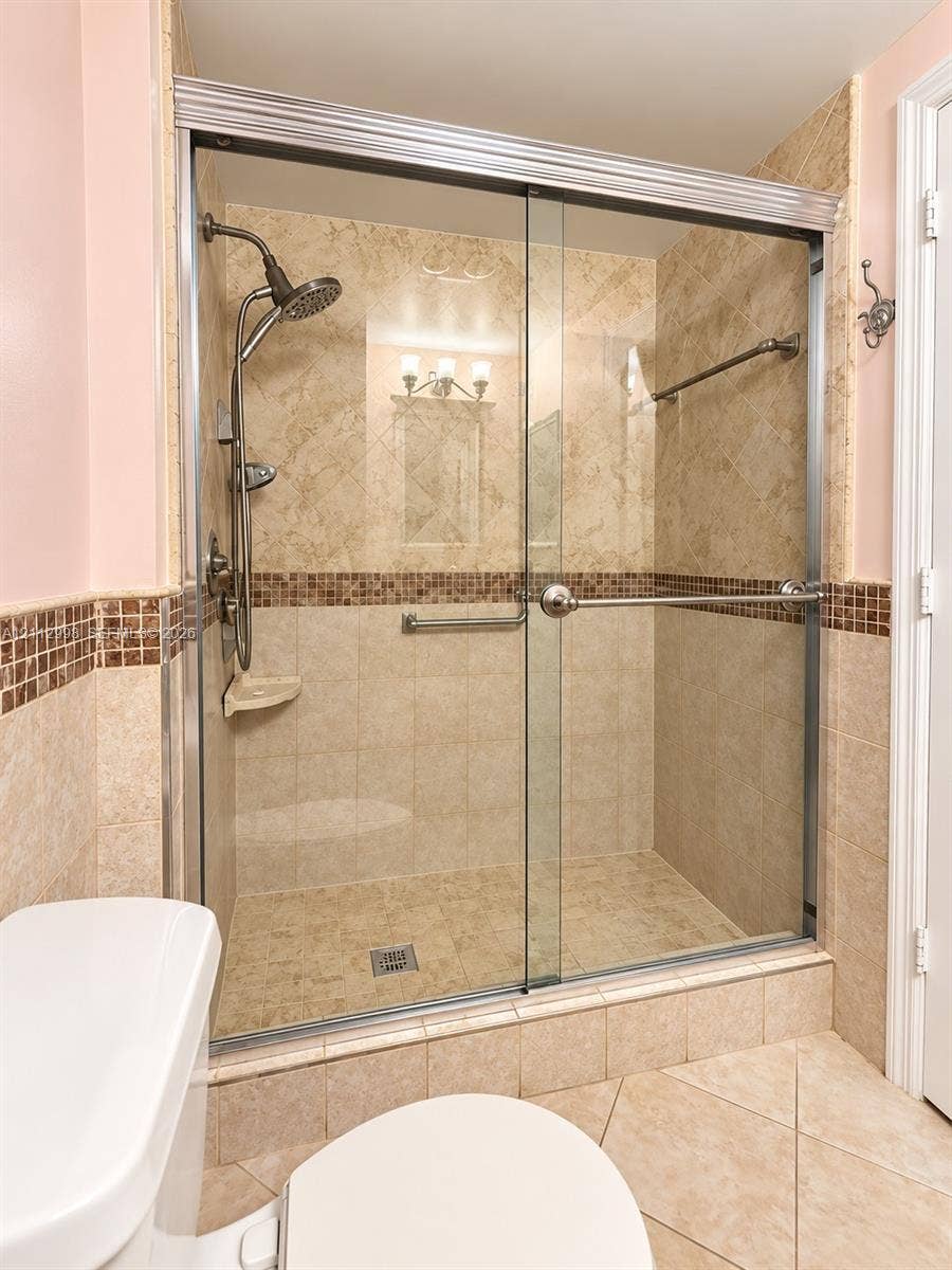 Walk-in shower featuring glass sliding doors, stone-tile surround with a decorative mosaic accent border, integrated soap ledge, and a polished chrome handheld shower fixture