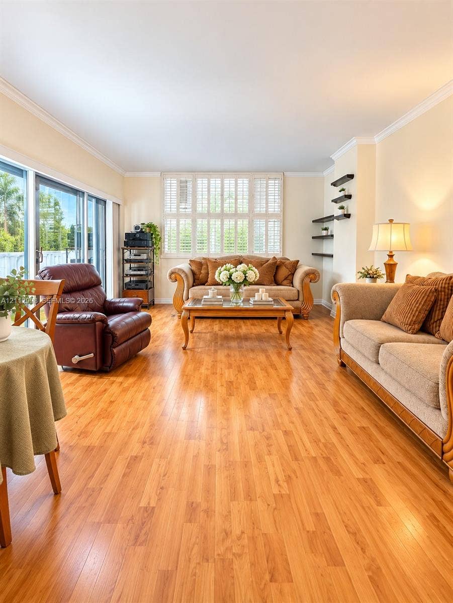 Living area featuring wood-finish flooring, sliding glass doors, crown molding, plantation shutters, and built-in wall shelving