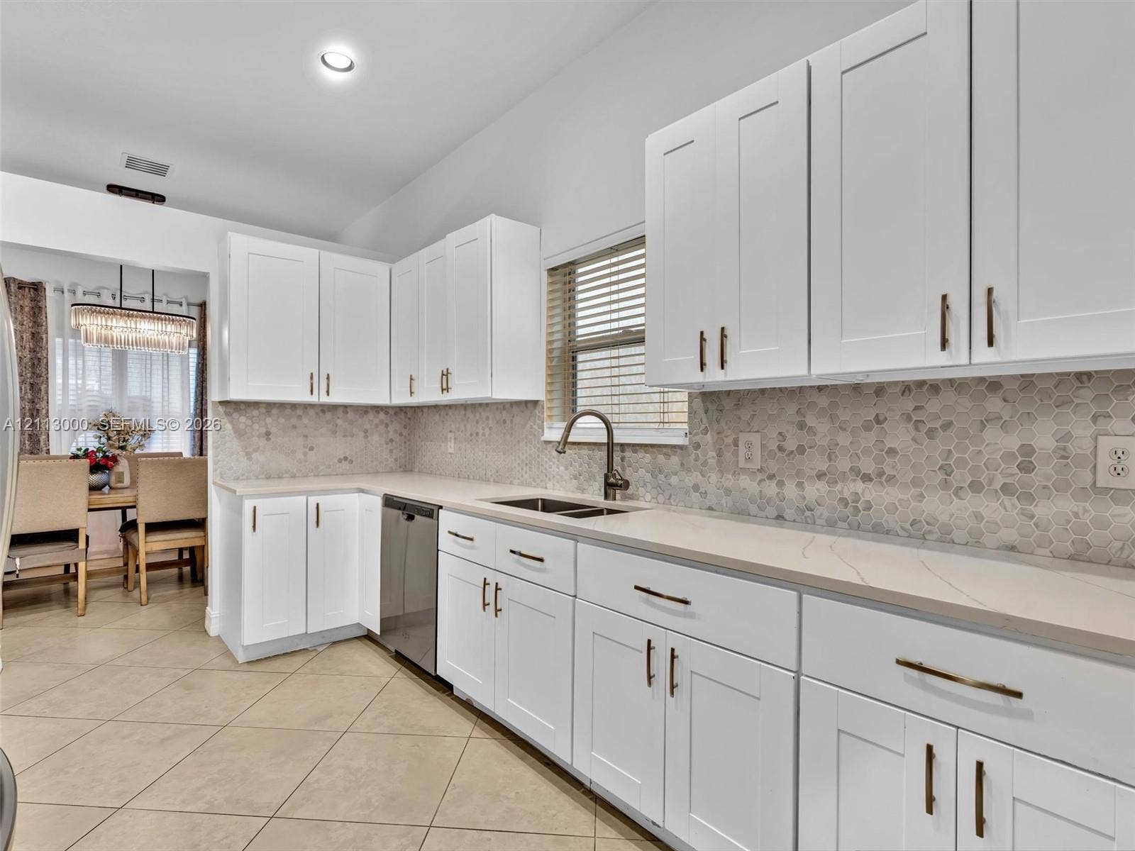 10860 La Salinas Circle, Boca Raton, FL 33428 White shaker-style cabinetry with metallic pulls, stone-look countertops, hexagonal tile backsplash, stainless steel dishwasher, and a gooseneck kitchen faucet