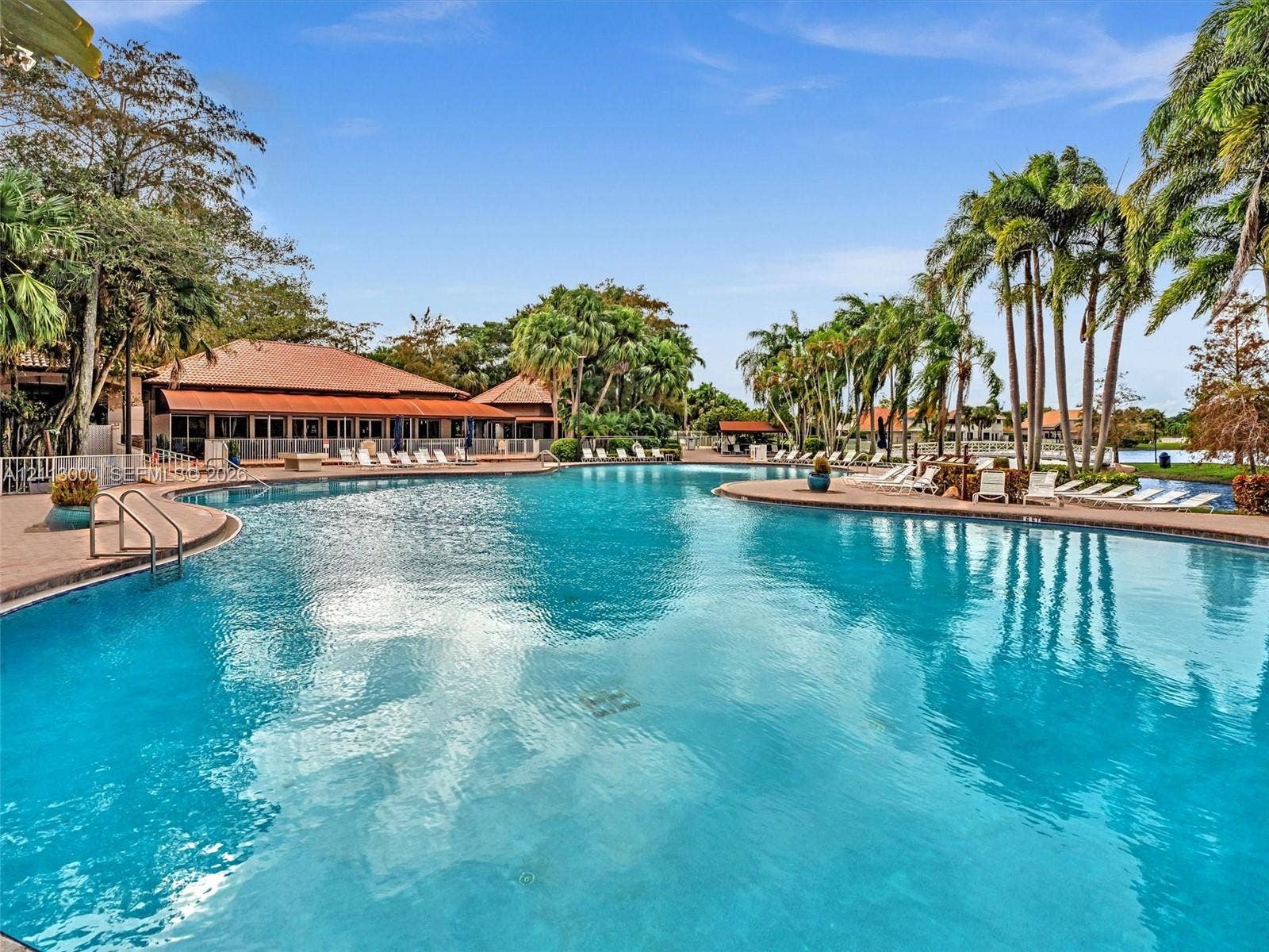 10860 La Salinas Circle, Boca Raton, FL 33428 Large free-form swimming pool featuring a tile border, metal handrails, a paved deck, and mature palm trees