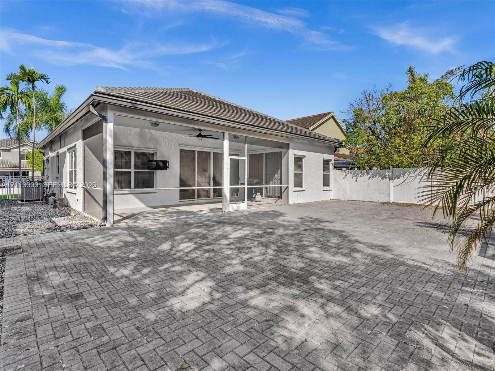 10860 La Salinas Circle, Boca Raton, FL 33428 Covered screened patio featuring a paver-stone floor, ceiling fan, and stucco exterior walls