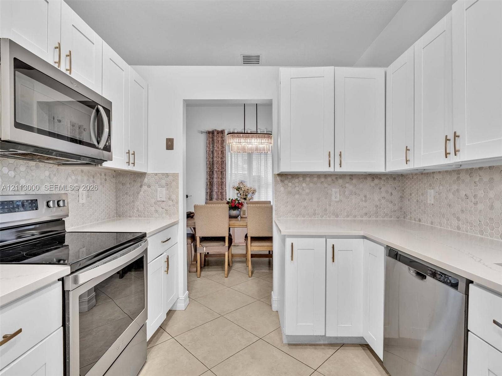 10860 La Salinas Circle, Boca Raton, FL 33428 Kitchen featuring white shaker-style cabinetry, stainless steel appliances, neutral stone-finish countertops, and a hexagonal tile backsplash