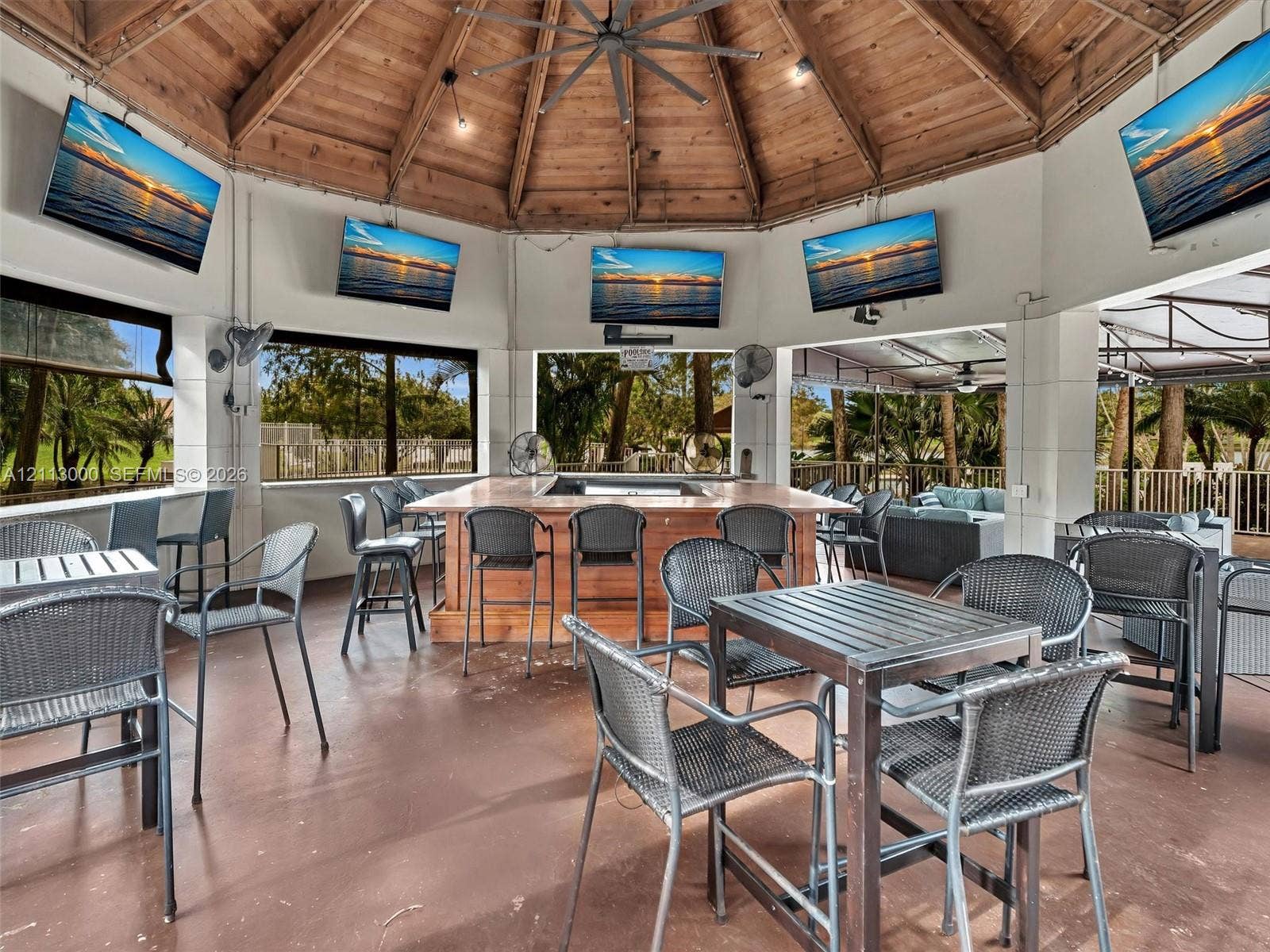 10860 La Salinas Circle, Boca Raton, FL 33428 Covered outdoor pavilion featuring a vaulted wood-beam ceiling, built-in center bar, stone-finish flooring, and multiple wall-mounted television screens