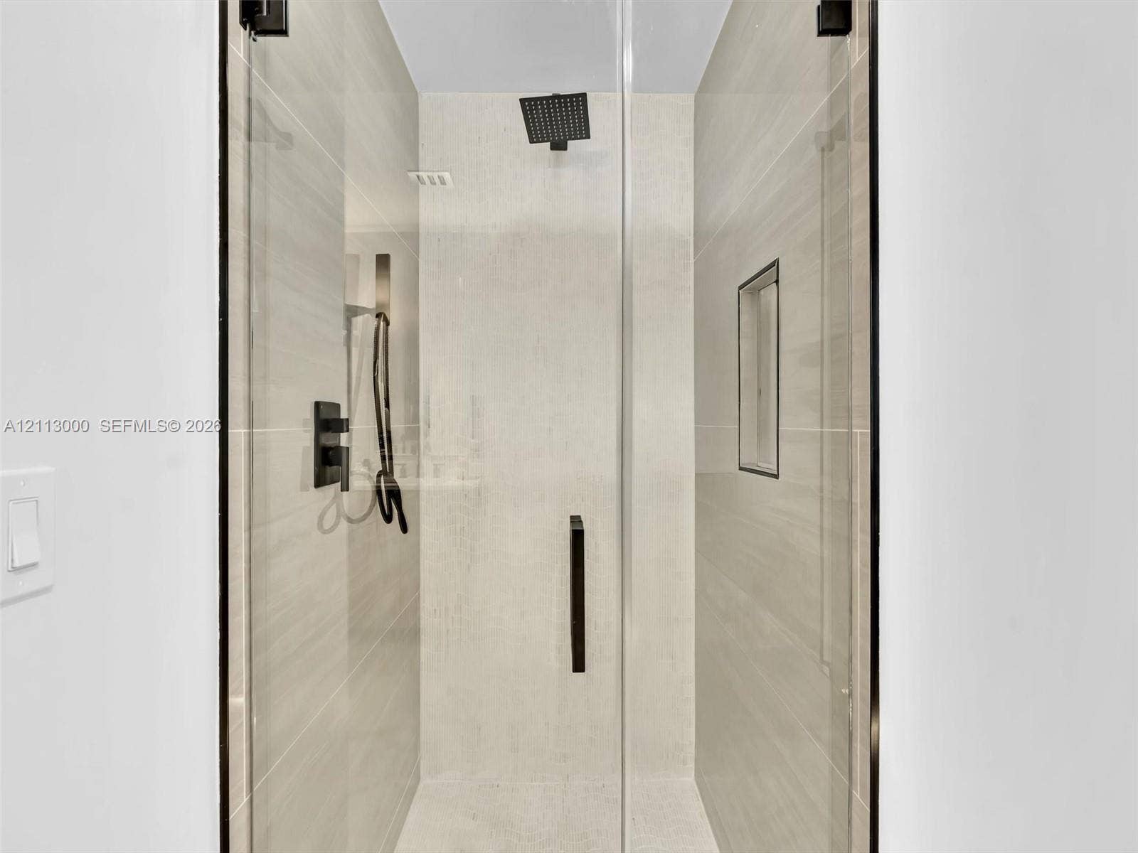 10860 La Salinas Circle, Boca Raton, FL 33428 Walk-in shower featuring floor-to-ceiling tile, frameless glass enclosure, matte black rainfall showerhead with handheld sprayer, and an integrated wall niche