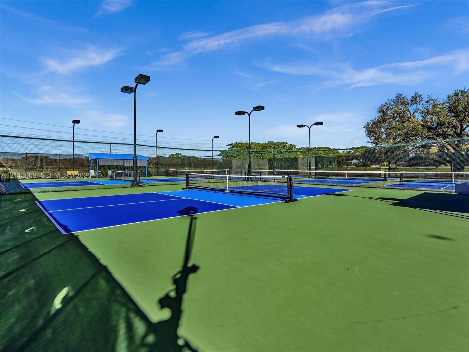 10860 La Salinas Circle, Boca Raton, FL 33428 Multi-court tennis facility featuring blue and green hardcourt surfaces, perimeter chain-link fencing, and overhead court lighting