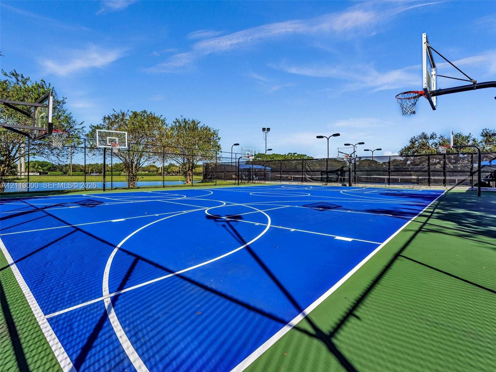 10860 La Salinas Circle, Boca Raton, FL 33428 Multi-purpose sports court featuring a high-performance surface, multiple basketball hoops, stadium-style lighting, and perimeter fencing