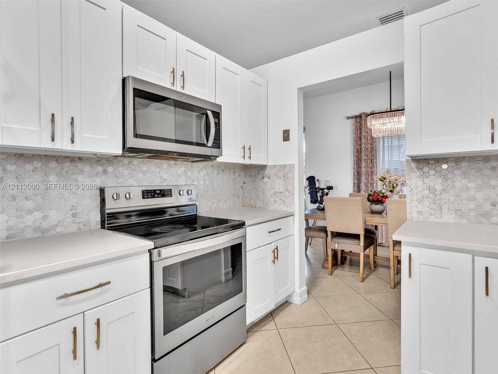 10860 La Salinas Circle, Boca Raton, FL 33428 Kitchen featuring white Shaker-style cabinetry, stainless steel appliances, hexagonal tile backsplash, solid-surface countertops, and tile flooring