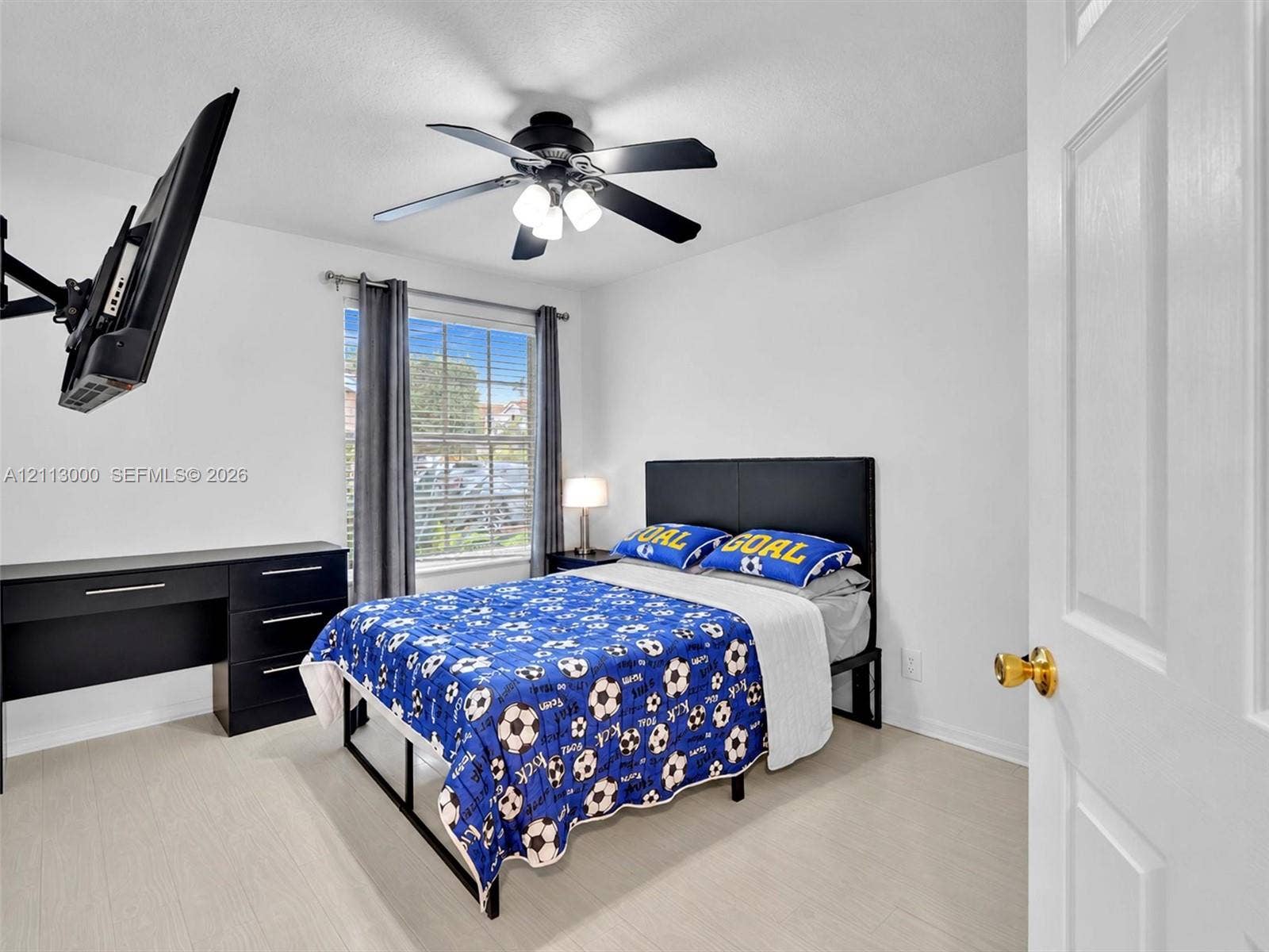 10860 La Salinas Circle, Boca Raton, FL 33428 Room featuring wood-finish flooring, a matte black multi-blade ceiling fan with integrated lighting, a dual-pane window, and a multi-panel door with brass-finish hardware
