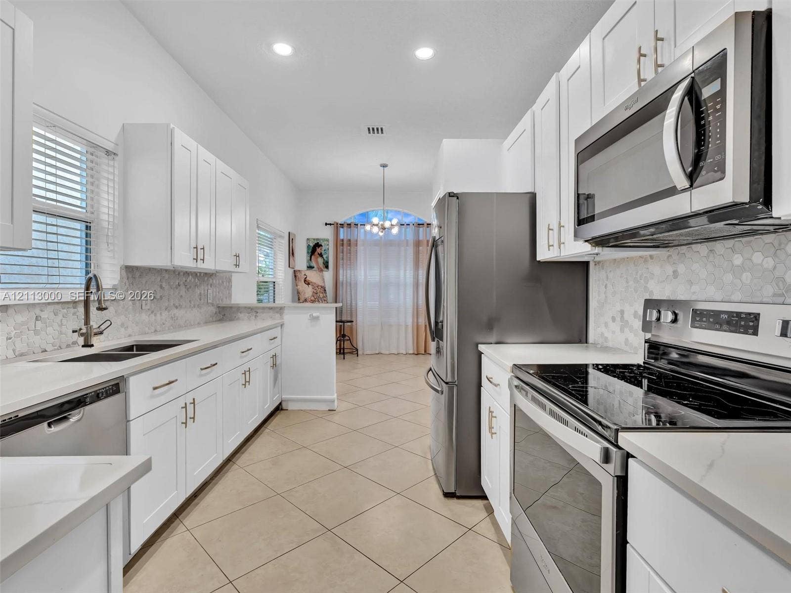 10860 La Salinas Circle, Boca Raton, FL 33428 Kitchen featuring white shaker-style cabinetry, stainless steel appliances, quartz countertops, hexagonal mosaic tile backsplash, and tile flooring