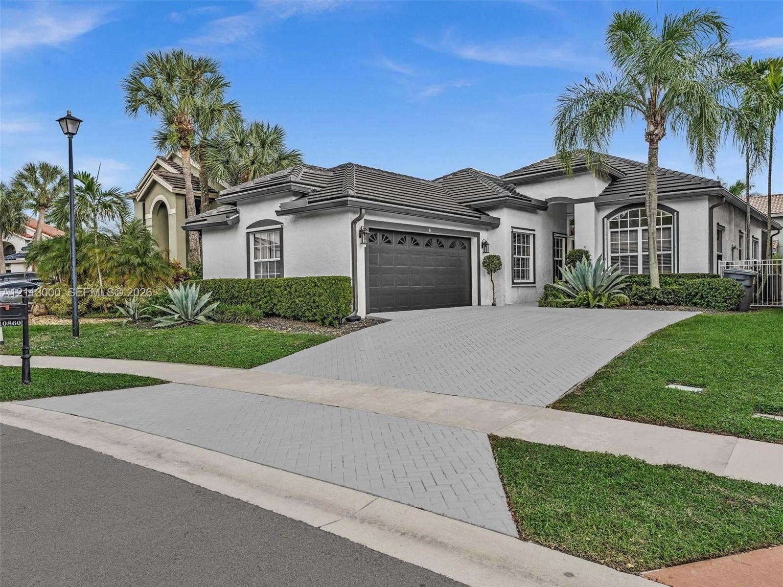 10860 La Salinas Circle, Boca Raton, FL 33428 Stucco exterior with a multi-hipped tile roof, decorative arched window accents, and a paved driveway leading to a two-car garage