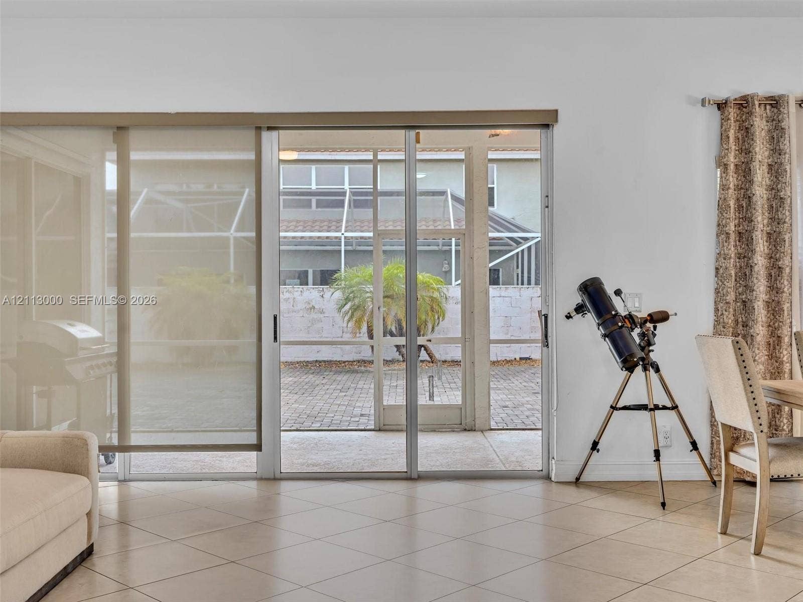 10860 La Salinas Circle, Boca Raton, FL 33428 Large-format sliding glass doors with neutral roller shades, ceramic tile flooring, and a screened-in patio featuring paver hardscaping
