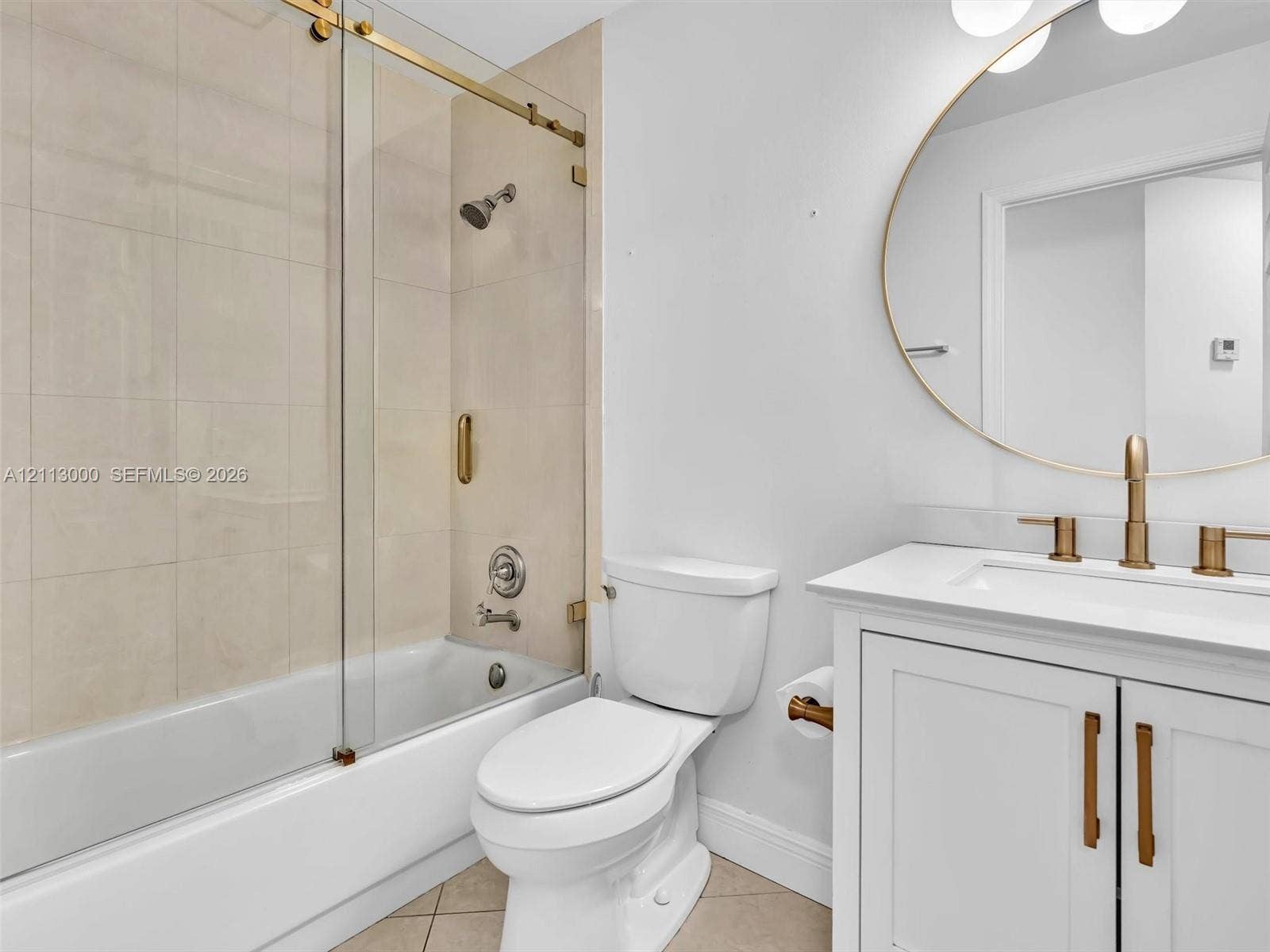 10860 La Salinas Circle, Boca Raton, FL 33428 Bathroom featuring a white vanity cabinet with a stone countertop, an oval mirror with gold-tone trim, gold-tone faucet and hardware, and a glass-enclosed tub shower with tile surround