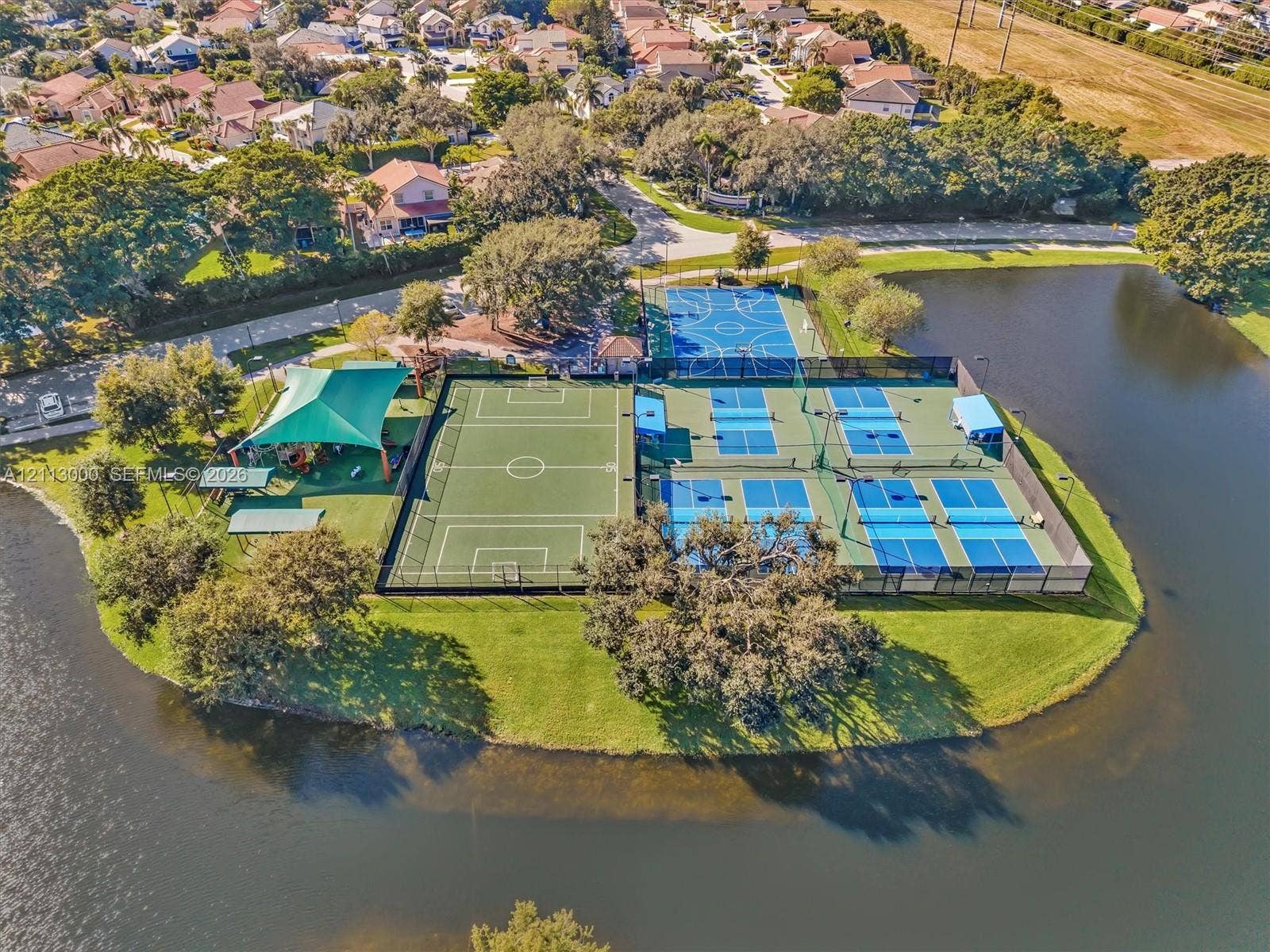 10860 La Salinas Circle, Boca Raton, FL 33428 Recreational complex featuring multi-purpose sports courts, pickleball courts, a soccer field, and a shaded playground pavilion situated on a waterfront parcel