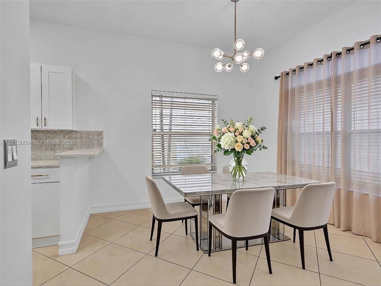 10860 La Salinas Circle, Boca Raton, FL 33428 Neutral-toned tile flooring, modern multi-globe chandelier, white shaker-style cabinetry, and large windows with horizontal blinds