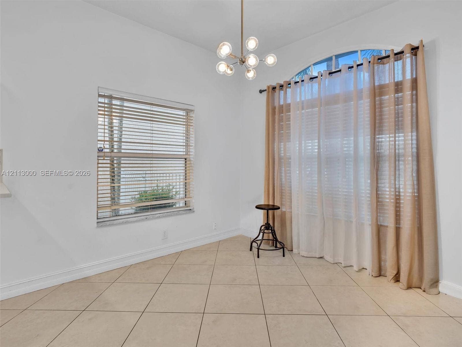 10860 La Salinas Circle, Boca Raton, FL 33428 High ceilings featuring a multi-globe chandelier, neutral tile flooring, a large arched window, and rectangular windows with horizontal blinds