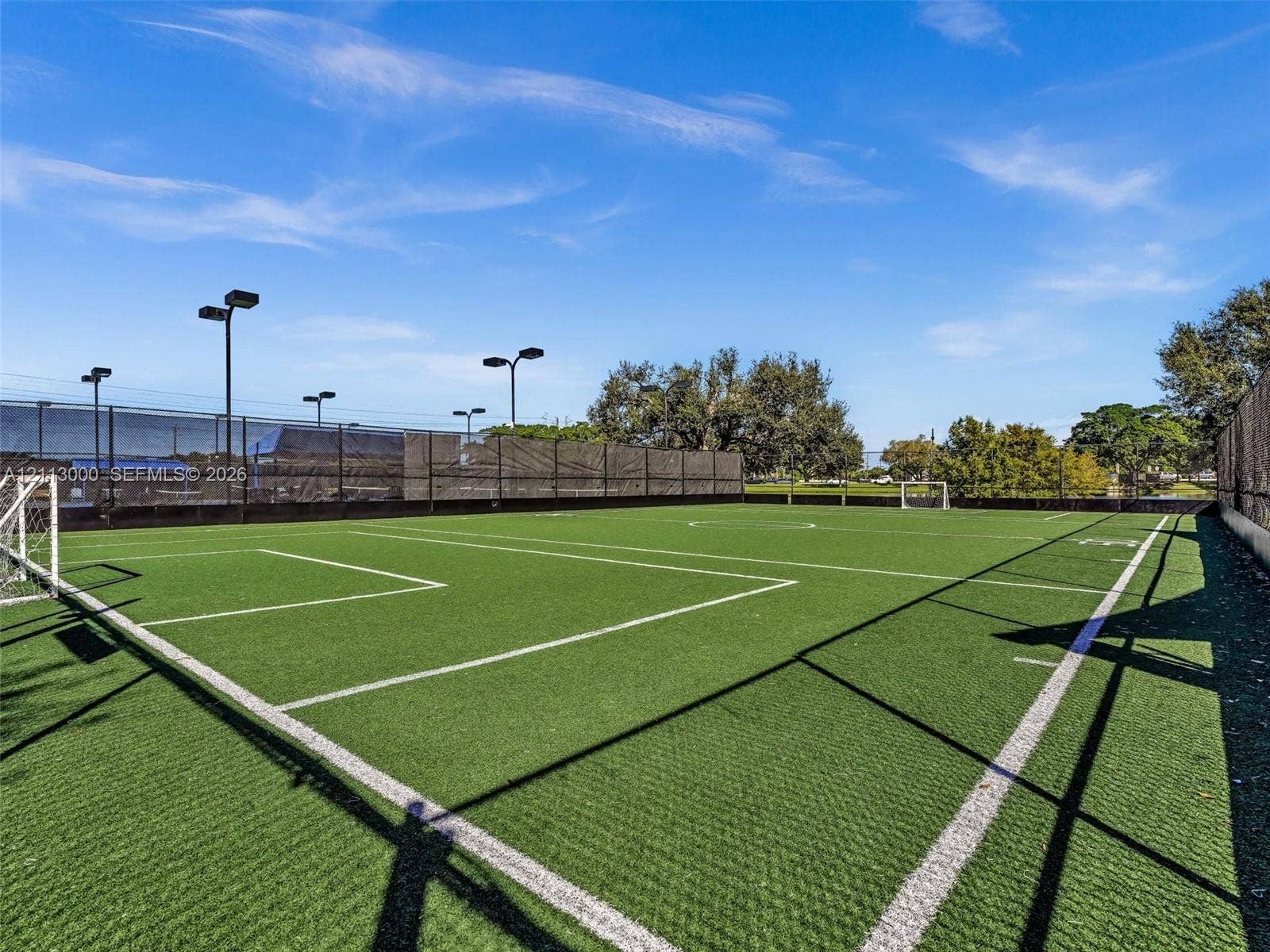 10860 La Salinas Circle, Boca Raton, FL 33428 Private sports court featuring synthetic turf, perimeter fencing, and integrated stadium-style lighting