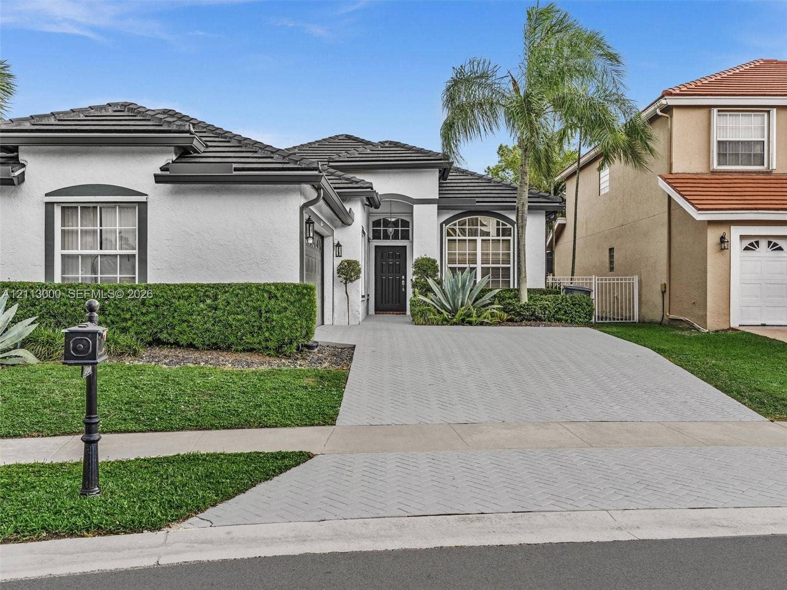 10860 La Salinas Circle, Boca Raton, FL 33428 Stucco exterior featuring a dark-toned tile roof, arched entryway, decorative arched windows, and a patterned paved driveway