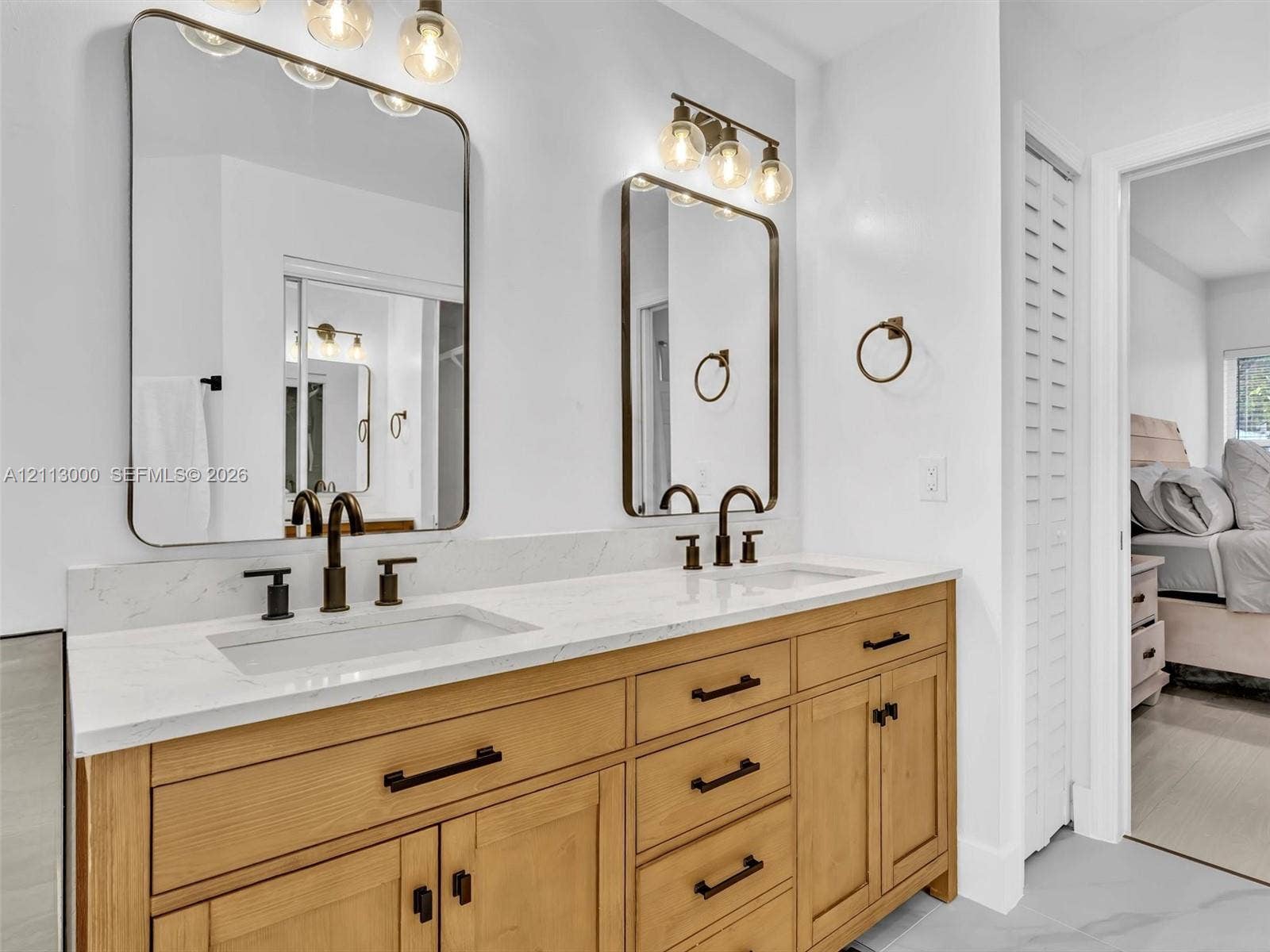 10860 La Salinas Circle, Boca Raton, FL 33428 Dual-sink vanity with a light wood-finish cabinet, stone-look countertop, integrated rectangular sinks, oil-rubbed bronze fixtures, and two rectangular wall-mounted mirrors with coordinating light fixtures