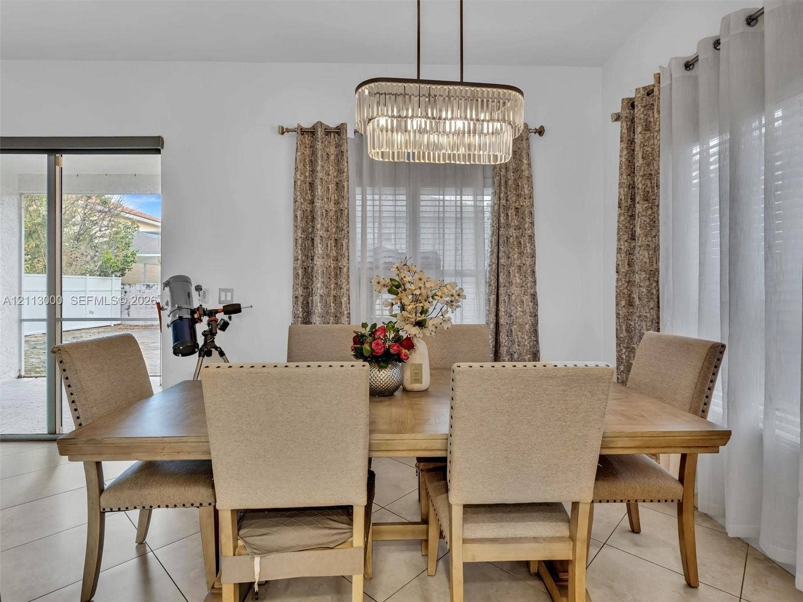 10860 La Salinas Circle, Boca Raton, FL 33428 Dining area featuring large-format tile flooring, a tiered crystal chandelier, and sliding glass doors providing outdoor access