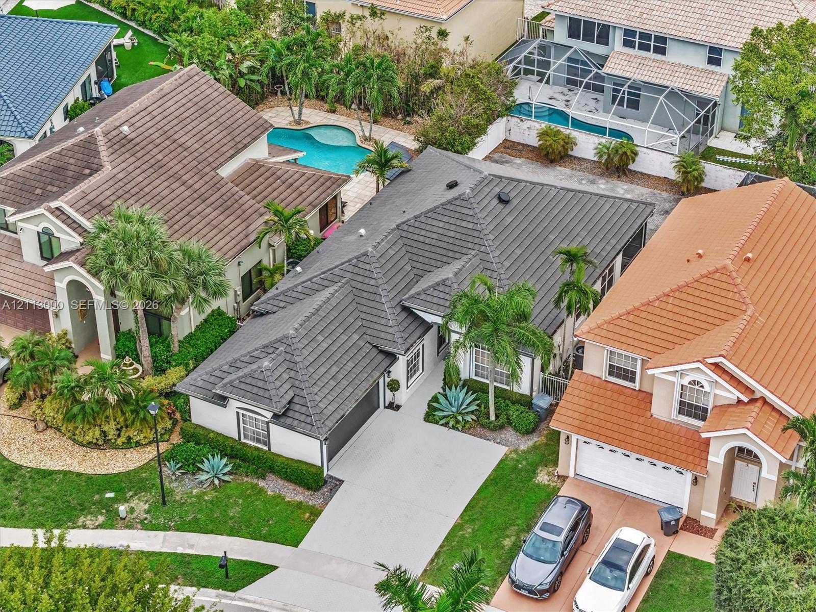 10860 La Salinas Circle, Boca Raton, FL 33428 Aerial view of a residential property featuring a dark-toned tile roof, attached two-car garage, concrete driveway, and landscaped front yard